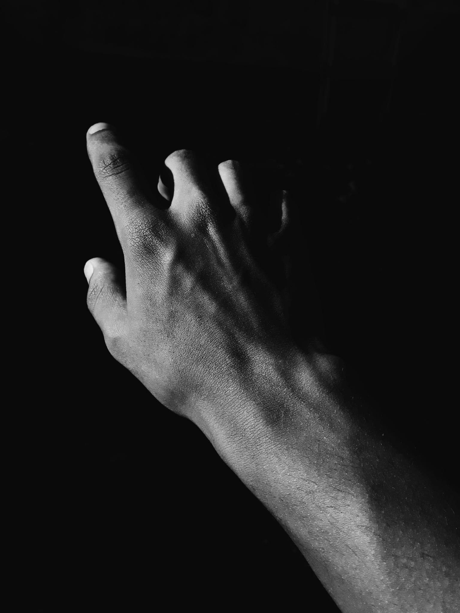 Black and white artistic photograph of a human hand reaching up with dramatic shadows.